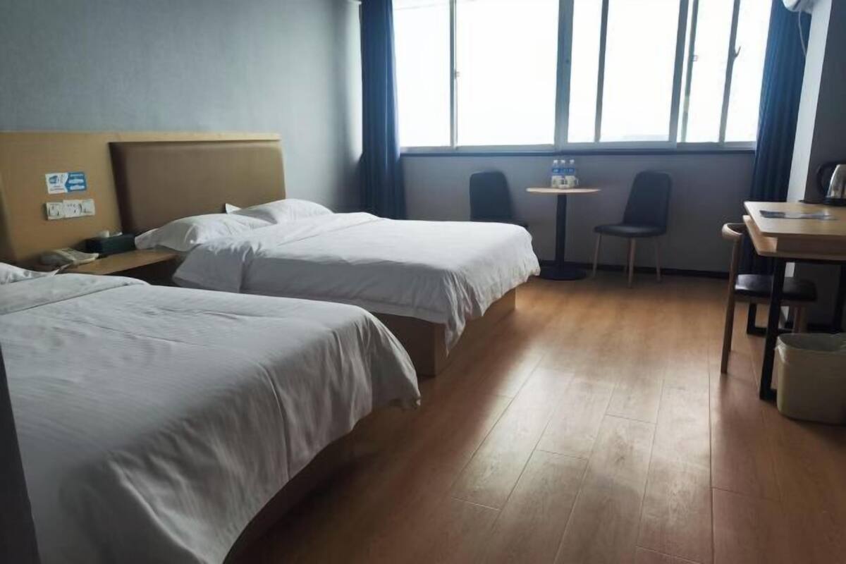 A hotel room with two beds, a desk, a chair, a small table, and a window with curtains.