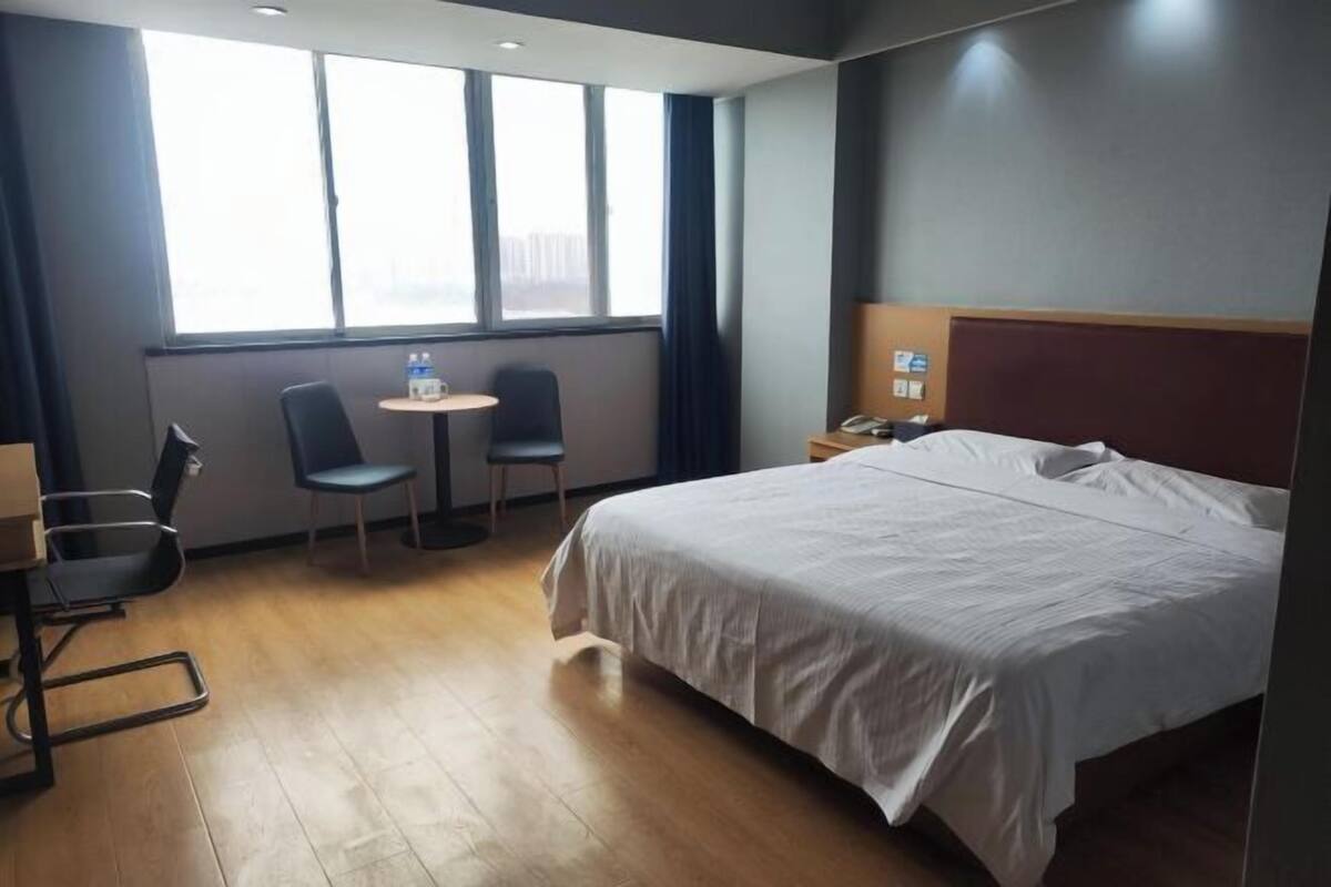 A hotel room with a large bed, a desk with two chairs, a small table, and a window with curtains.