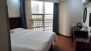 A hotel room with a bed, a desk with a chair, a small table, a window with curtains, and a view of buildings outside. - GreenTree Inn Express Hotel (Suqian Xiangwang East Road Suyu Bureau of Education Branch) (Suqian)