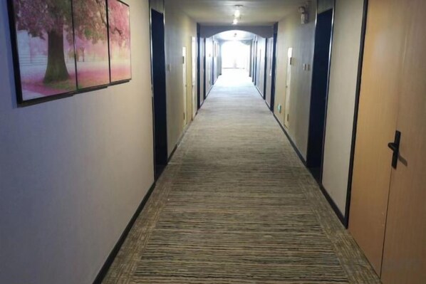 A hotel hallway with a carpeted floor, doors on both sides, and a corridor leading to a bright end.