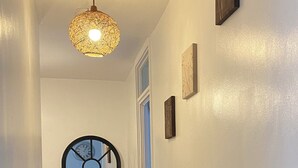 Een gang met een houten vloer, een plafondlamp, een raam met zwarte omlijsting, en een deur.