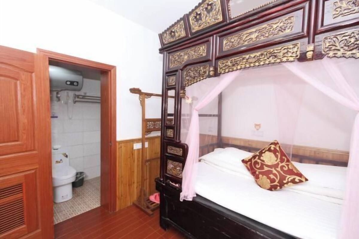 Une chambre à coucher avec un lit à baldaquin, une armoire en bois et une salle de bain équipée de toilettes et d’un lavabo.