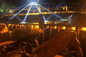 A nighttime view of a riverside restaurant with illuminated tables and a boat docked nearby. - Kelaiju Inn (Suzhou)