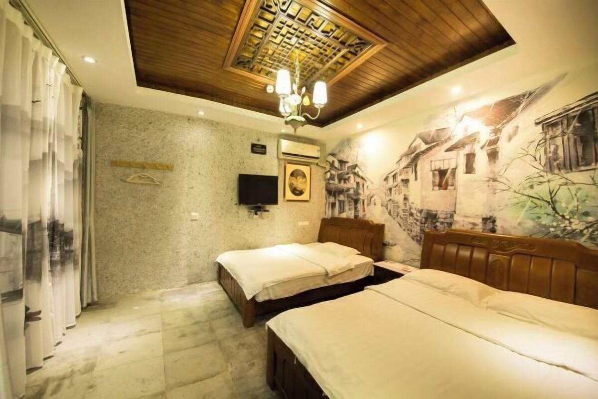 Une chambre avec deux lits, un plafond en bois, un téléviseur fixé au mur et une fresque murale.