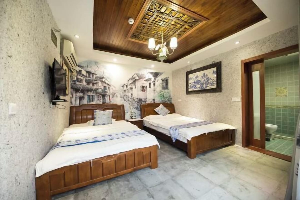 A bedroom with two wooden beds, a chandelier, and a mural of a street scene on the wall.