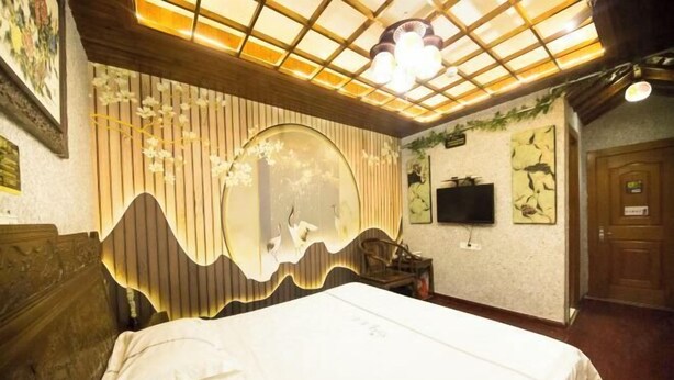 A bedroom with a bed, a large mirror, a television, and a wooden door. - Kelaiju Inn (Suzhou)
