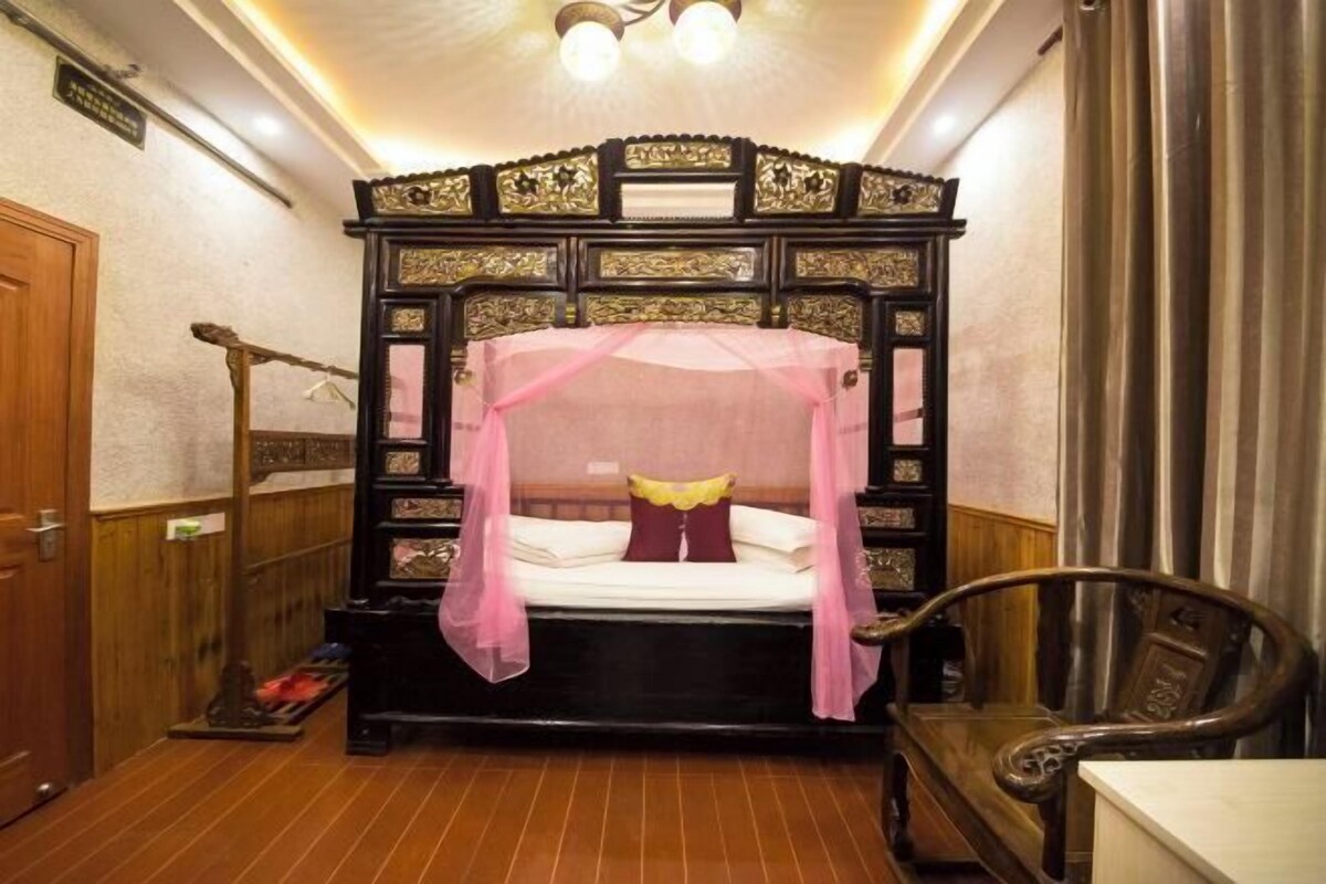 A traditional room with a four-poster bed, a wooden chair, and a small table.