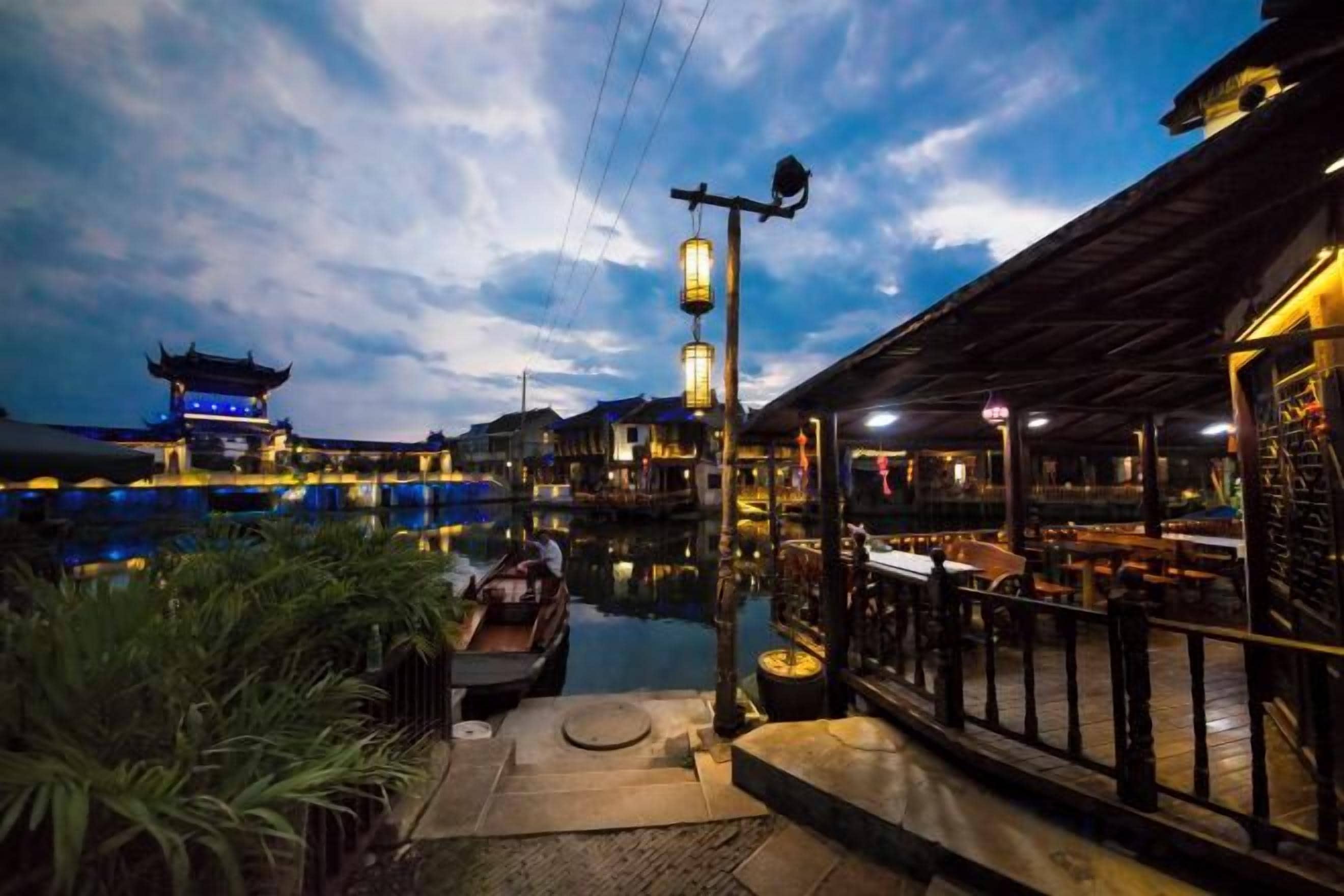 Un restaurante a la orilla del río con terraza, un edificio tradicional al fondo y cielo despejado.