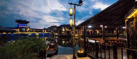 Un restaurante a la orilla del río con terraza, un edificio tradicional al fondo y cielo despejado.