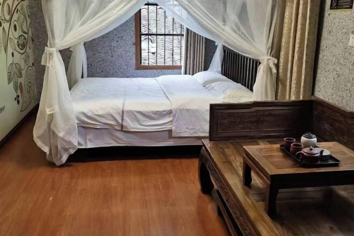 Une chambre à coucher avec un lit sous un dais, une table en bois avec des tasses et une théière, et une fenêtre avec des barreaux.