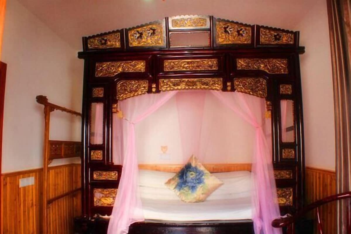 A bed with a canopy, a wooden headboard with intricate carvings, and a single decorative pillow.