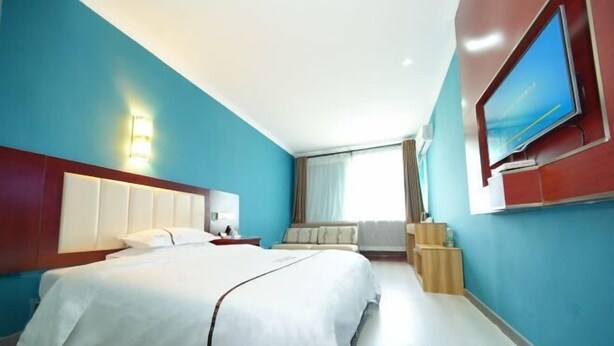 A hotel room with a large bed, a TV mounted on the wall, and a window with curtains. - Jinghe Heli Hotel (Jinghe)
