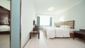 A hotel room with a bed, bedside tables, a desk, and a view of the city. - Jinghe Heli Hotel (Jinghe)