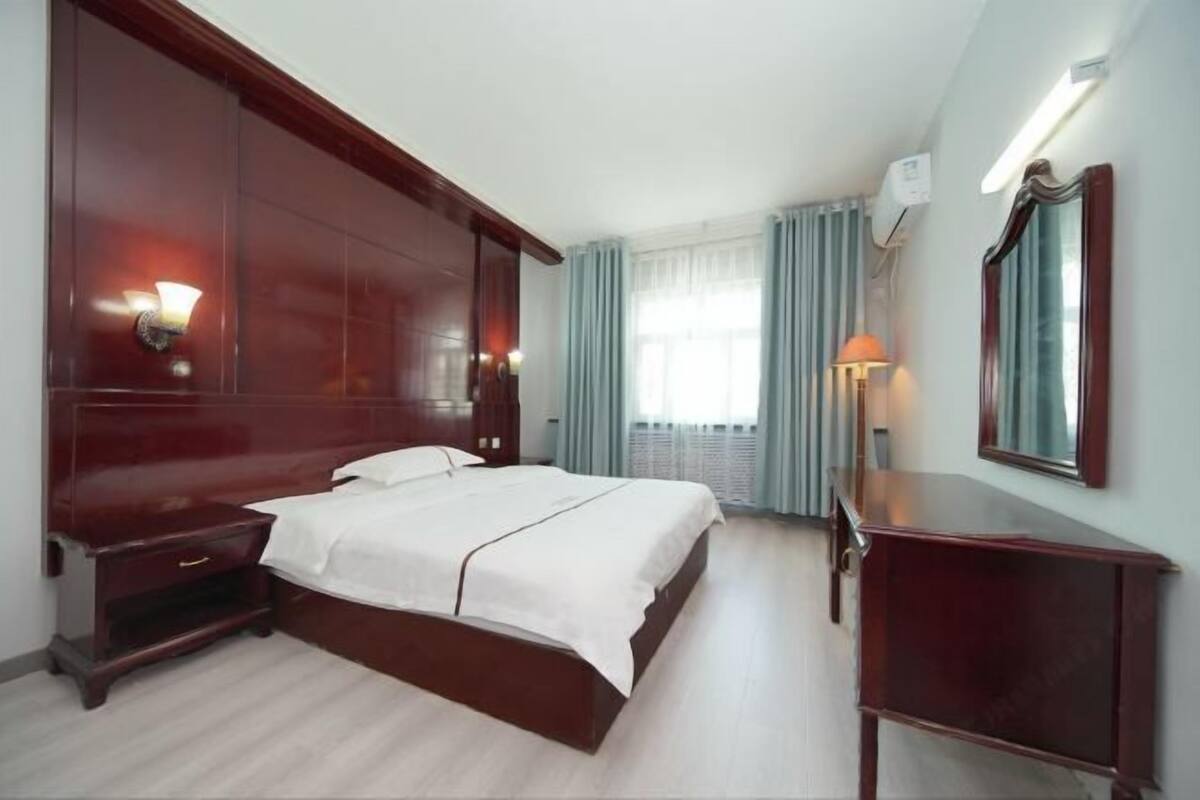 Una camera d'albergo con un letto grande, un comodino, una cassettiera, uno specchio e una finestra con tende.