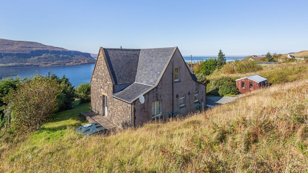 A stone house with a sloped roof, a small shed, and a view of a lake and hills. - 3 bedroom accommodation in Waternish, Isle of Skye (Waternish, Isle of Skye)