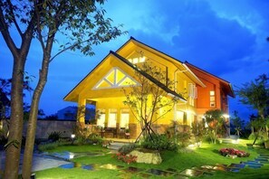 Ein modernes Haus mit einer großen Veranda, einem gepflegten Garten und einem wolkenlosen Himmel.