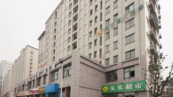 Un edificio de varios pisos con un local comercial en la planta baja, con un letrero verde con texto blanco, y un cielo despejado arriba.