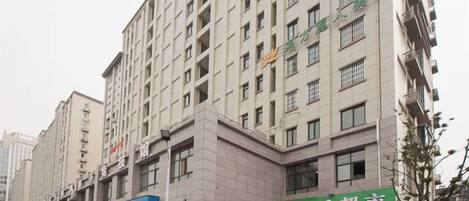 A multi-story building with a commercial ground floor, featuring a green sign with white text, and a clear sky above.