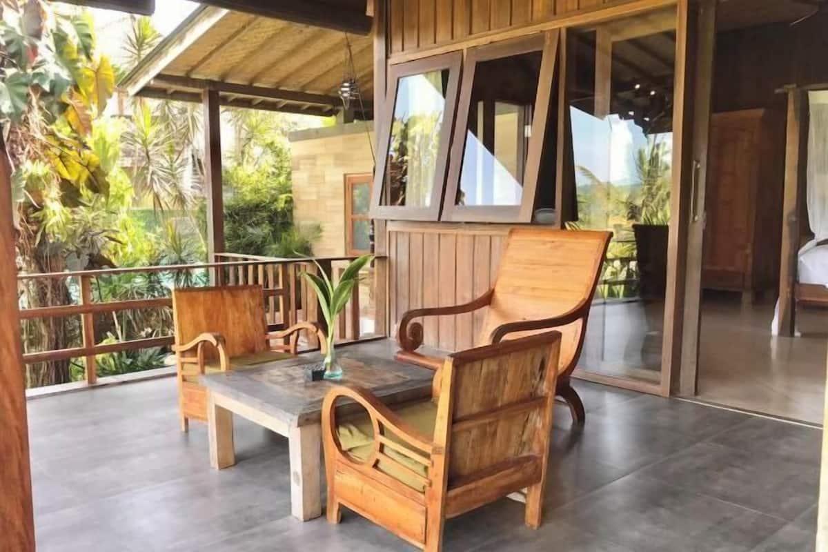 Een houten terras met een tafel en stoelen, omgeven door weelderig groen.