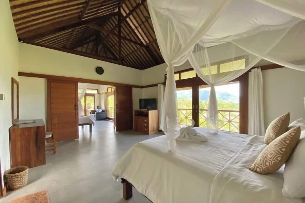 Een slaapkamer met een bed, witte gordijnen en uitzicht op de omgeving.