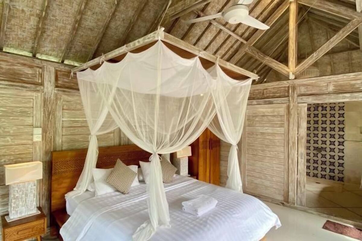 Een kamer met een bed dat door een hemelbed wordt overdekt, houten wanden en een deur met een patroon.