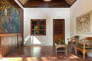 A hallway with a tiled floor, a wooden door labeled "DG 2", a window with a view, and a painting on the wall. - Sawah Indah Villa (Bali)