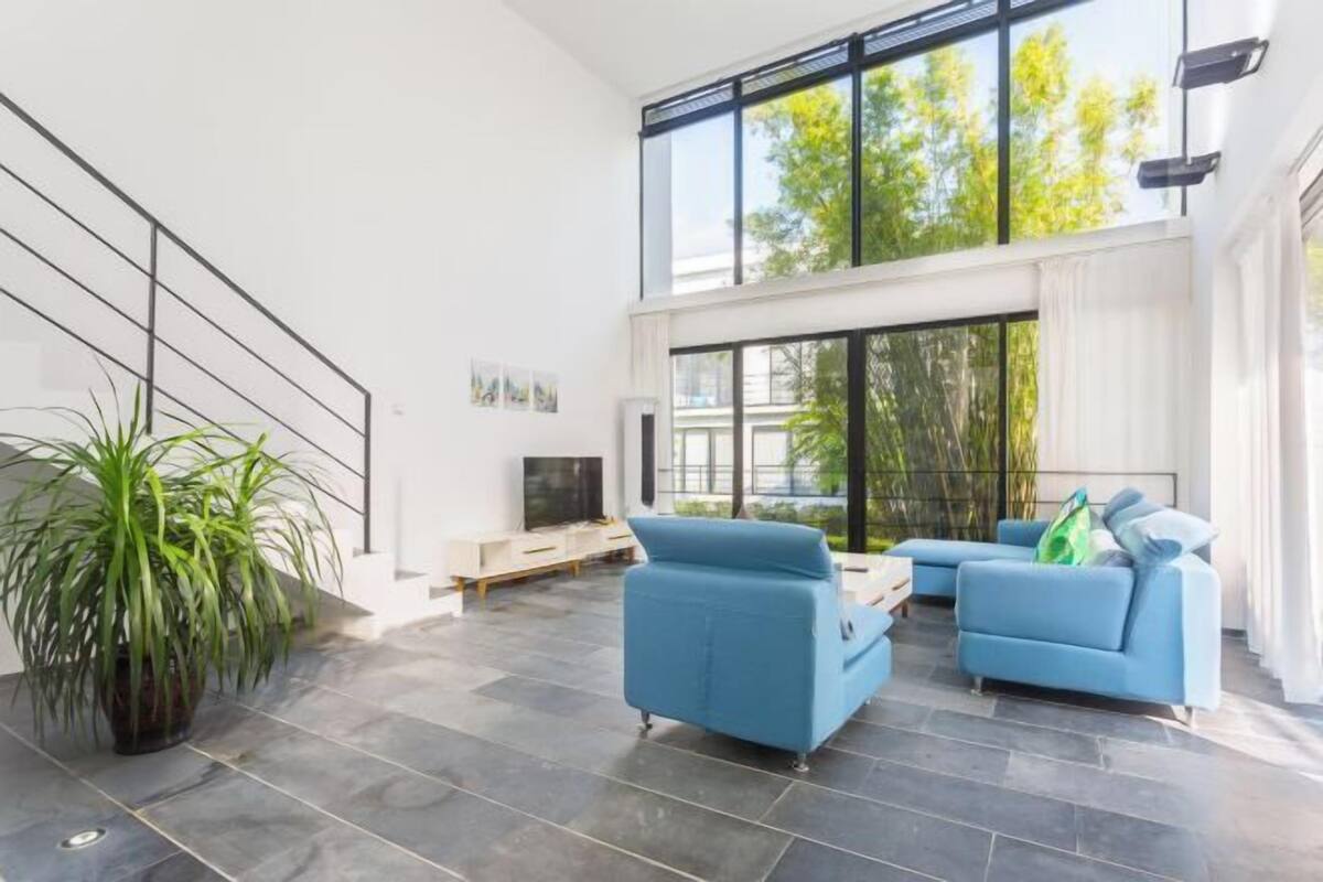Een moderne woonkamer met een groot raam, een trap en een potplant.