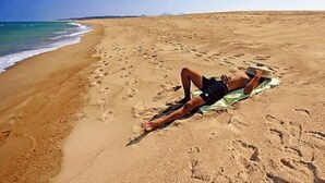 Una persona recostada sobre una toalla en una playa arenosa, con huellas en la arena.