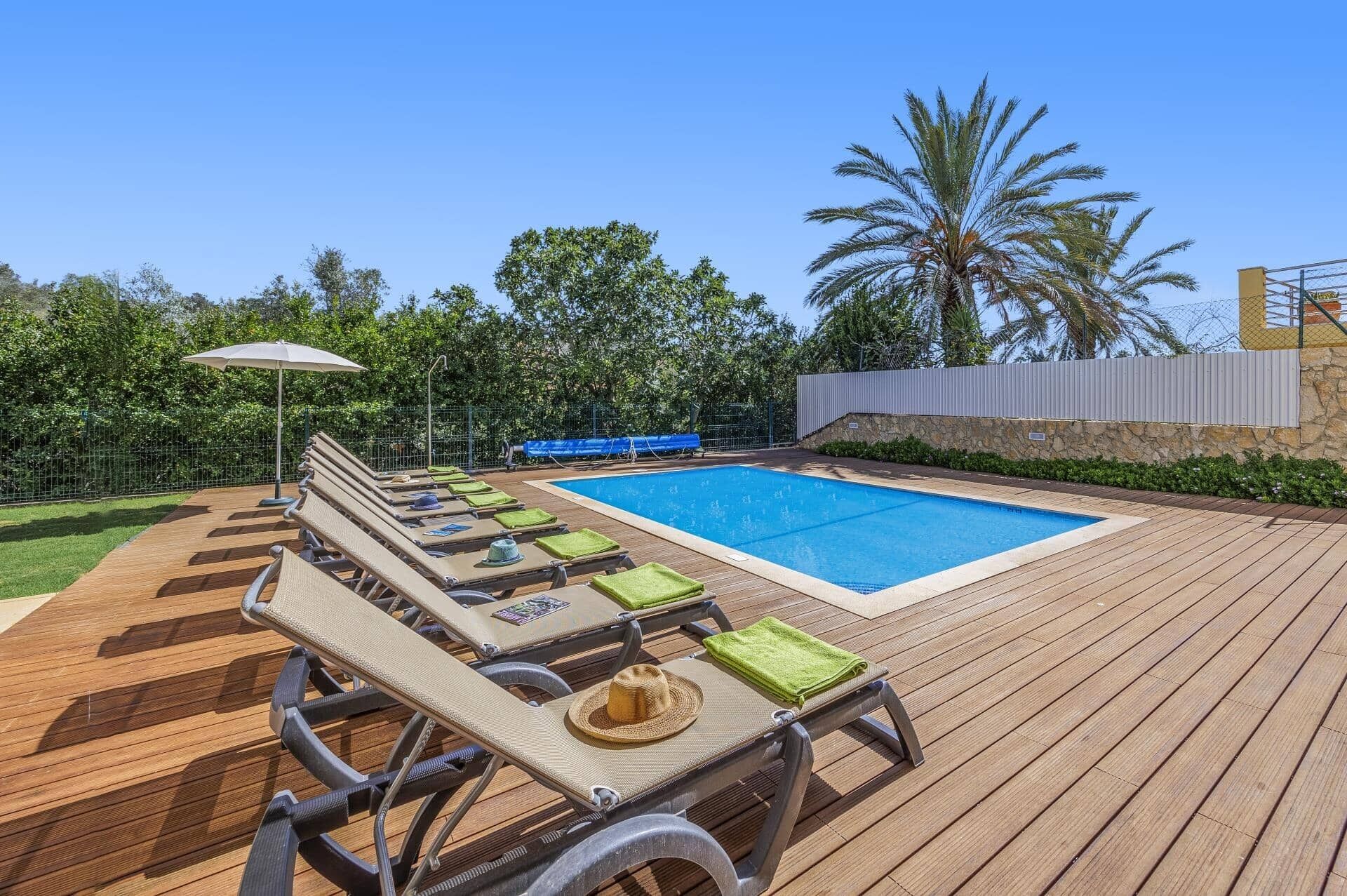 Una terraza de madera con sillones de descanso y una piscina.