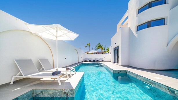 Un área de piscina moderna con sillones de descanso y una sombrilla blanca.