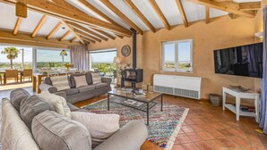 A spacious living area with a high ceiling, wooden beams, a fireplace, a television, and a view of the outdoors. - Villa Casa Moinho Azul by Villa Plus (Praia do Carvoeiro)