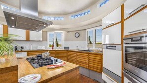 A modern kitchen with a central island, built-in appliances, and a curved ceiling. - Villa Casa Moinho Azul by Villa Plus (Praia do Carvoeiro)