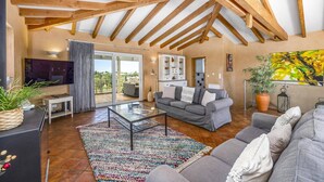 A spacious living room with a high ceiling, a grey sofa, a coffee table, and a large window offering a view of the outdoors. - Villa Casa Moinho Azul by Villa Plus (Praia do Carvoeiro)