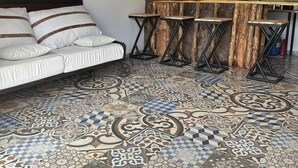 Ein Zimmer mit schrägem Dach, einer Couch mit gestreifter Polsterung, einem Holztisch mit Hockern und einem gemusterten Boden.