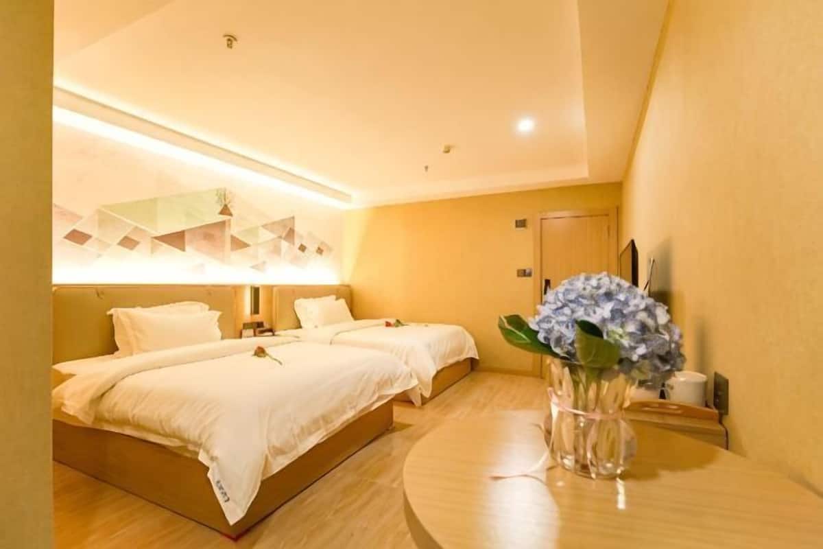 Une chambre d’hôtel avec deux lits, une table ronde, un vase avec des fleurs et un luminaire moderne.