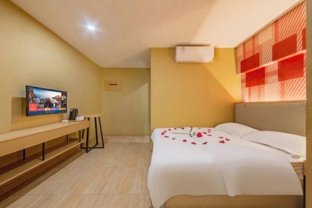 A hotel room with a bed, a TV on a stand, a small table, and a wall-mounted air conditioner.