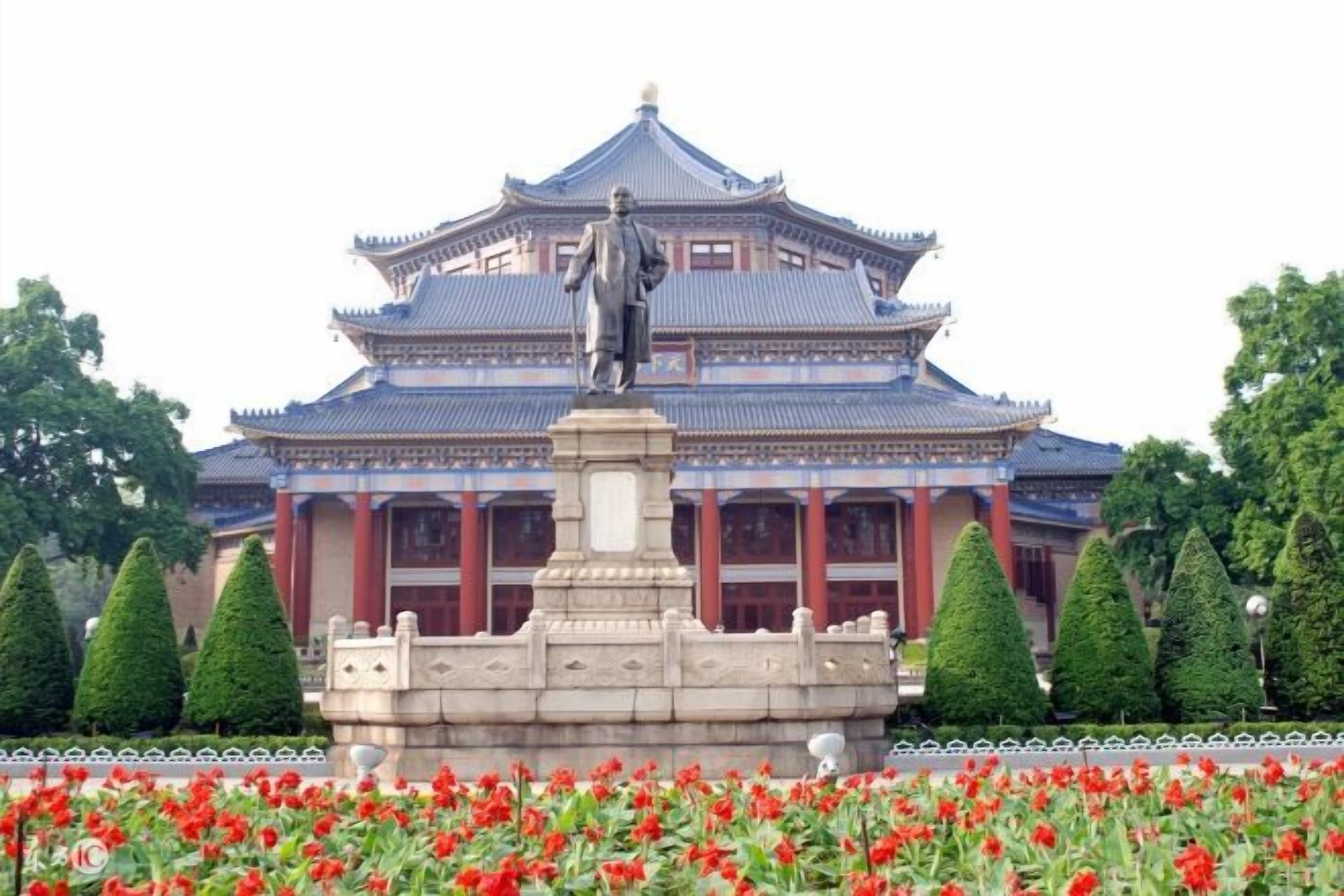 A traditional building with a statue in front, surrounded by a well-maintained garden with red flowers.