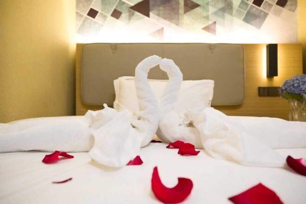 A hotel room with a neatly made bed, a headboard, and a wall-mounted light fixture.