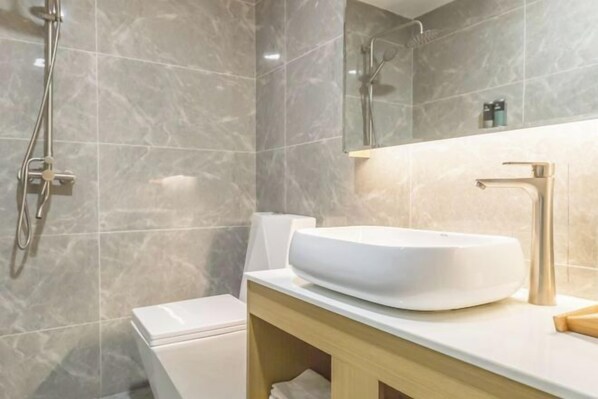 A bathroom with a white toilet, a vessel sink, a handheld showerhead, and a mirror above the sink. - Yuebei Hotel (Guangzhou)