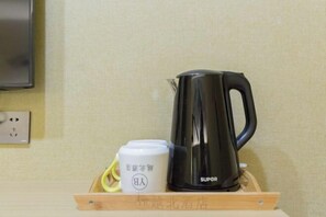 A black electric kettle and a white mug with a logo on a wooden tray. - Yuebei Hotel (Guangzhou)