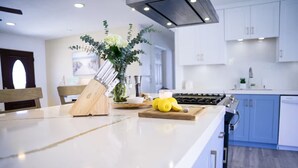 A modern kitchen with a marble countertop, a knife block, a cutting board with lemons, and a vase with flowers. - 8ft Deep Heated Pool, 9 Seat Medical Grade Jacuzzi, Mini-Golf & Chef’s Kitchen! (San Diego)