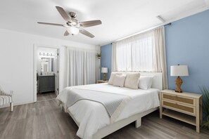 A bedroom with a bed, nightstands, a ceiling fan, and a bathroom visible through an open door. - 8ft Deep Heated Pool, 9 Seat Medical Grade Jacuzzi, Mini-Golf & Chef’s Kitchen! (San Diego)