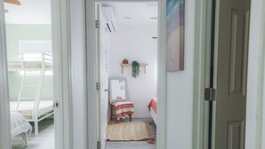 A narrow hallway leading to a bedroom with a bunk bed, a bedside table, a hanging plant, and a door. - 8ft Deep Heated Pool, 9 Seat Medical Grade Jacuzzi, Mini-Golf & Chef’s Kitchen! (San Diego)