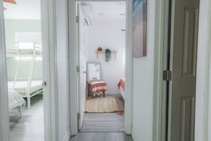A narrow hallway leading to a bedroom with a bunk bed, a bedside table, a hanging plant, and a door. - 8ft Deep Heated Pool, 9 Seat Medical Grade Jacuzzi, Mini-Golf & Chef’s Kitchen! (San Diego)