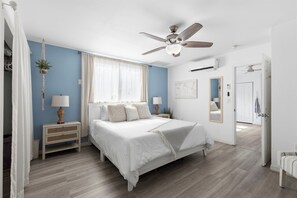 A bedroom with a bed, nightstands, a ceiling fan, a window with curtains, a world map on the wall, and a door leading to another room. - 8ft Deep Heated Pool, 9 Seat Medical Grade Jacuzzi, Mini-Golf & Chef’s Kitchen! (San Diego)