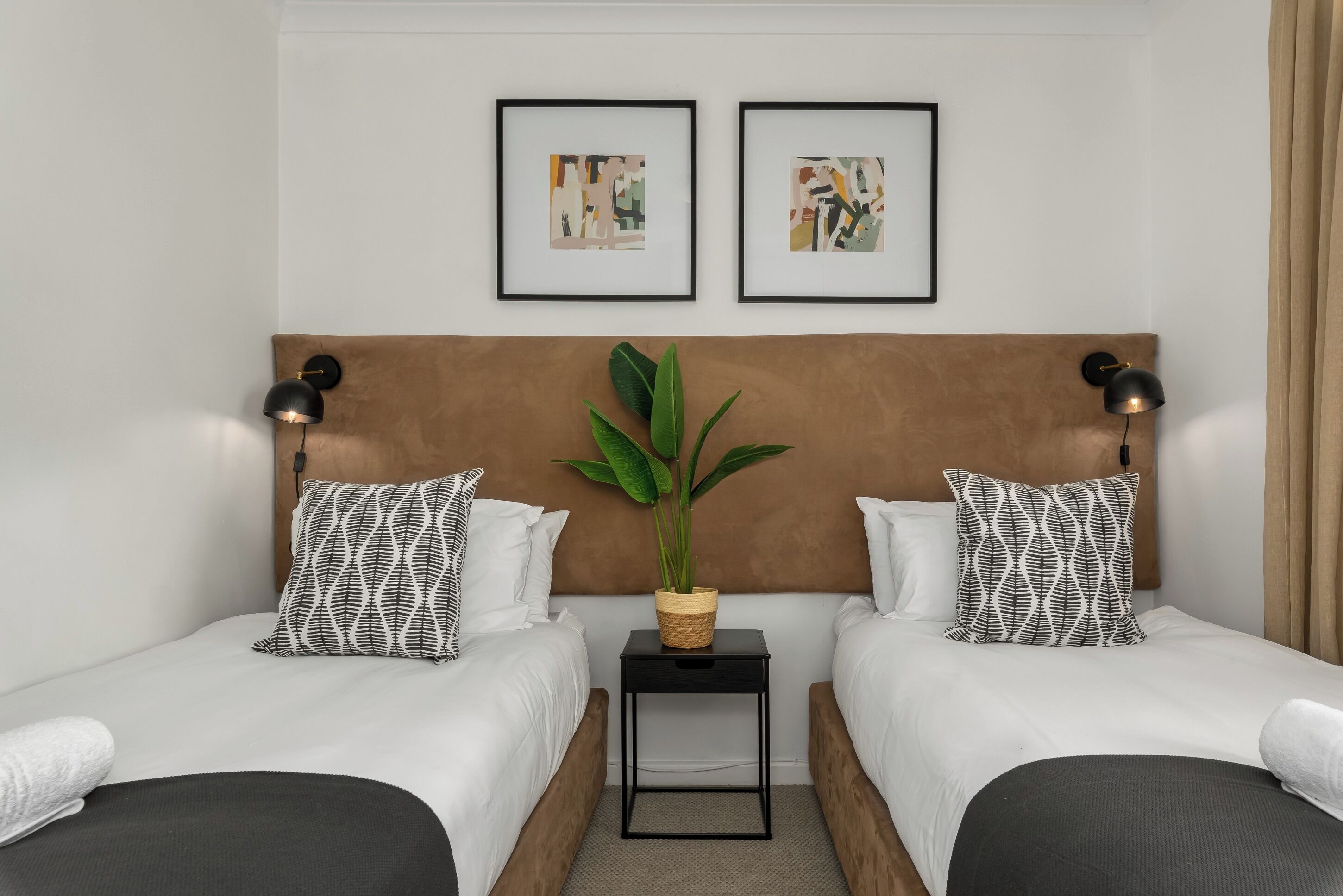 Habitación de hotel con dos camas, una mesita de noche con una planta y una obra de arte en la pared.