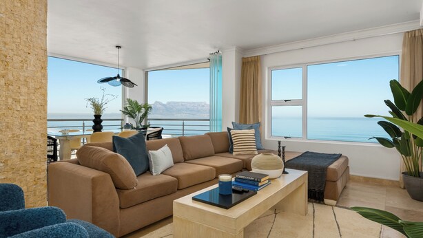Una sala de estar moderna con un ventanal grande, un sofá, una mesa de centro y vista al mar.
