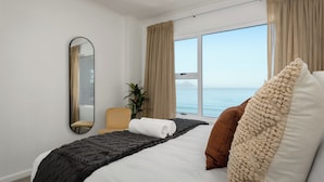 Habitación de hotel con cama, una silla, un espejo grande y vista al mar.