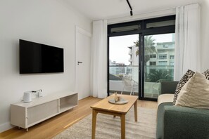 A modern living room with a flat-screen TV mounted on the wall, a wooden coffee table, a sofa, and a sliding glass door leading to a balcony. - The Sage - Designer Studio in Vibrant Sea Point (Cape Town)