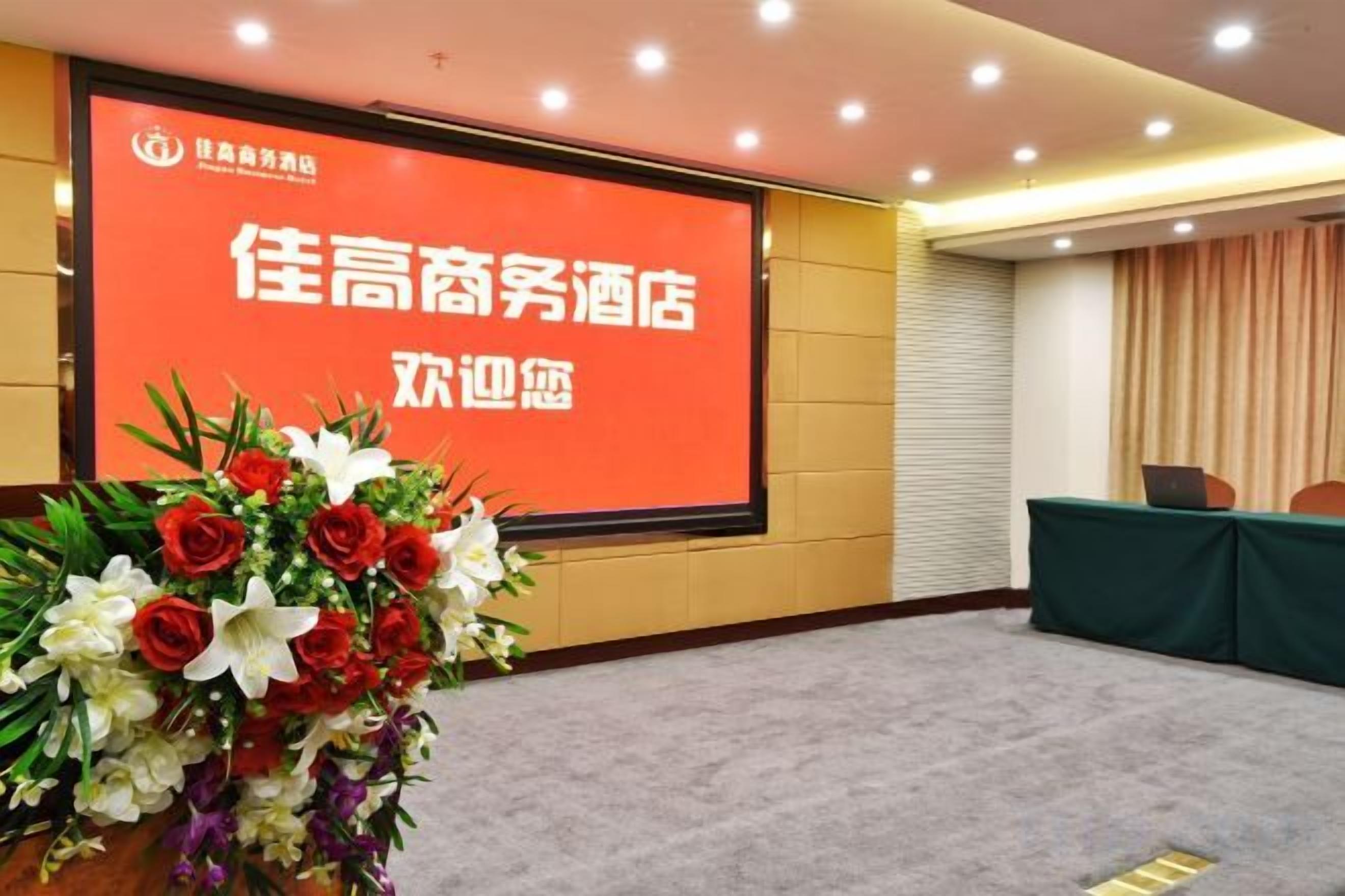A conference room with a large screen displaying text, a floral arrangement, and a table with chairs.